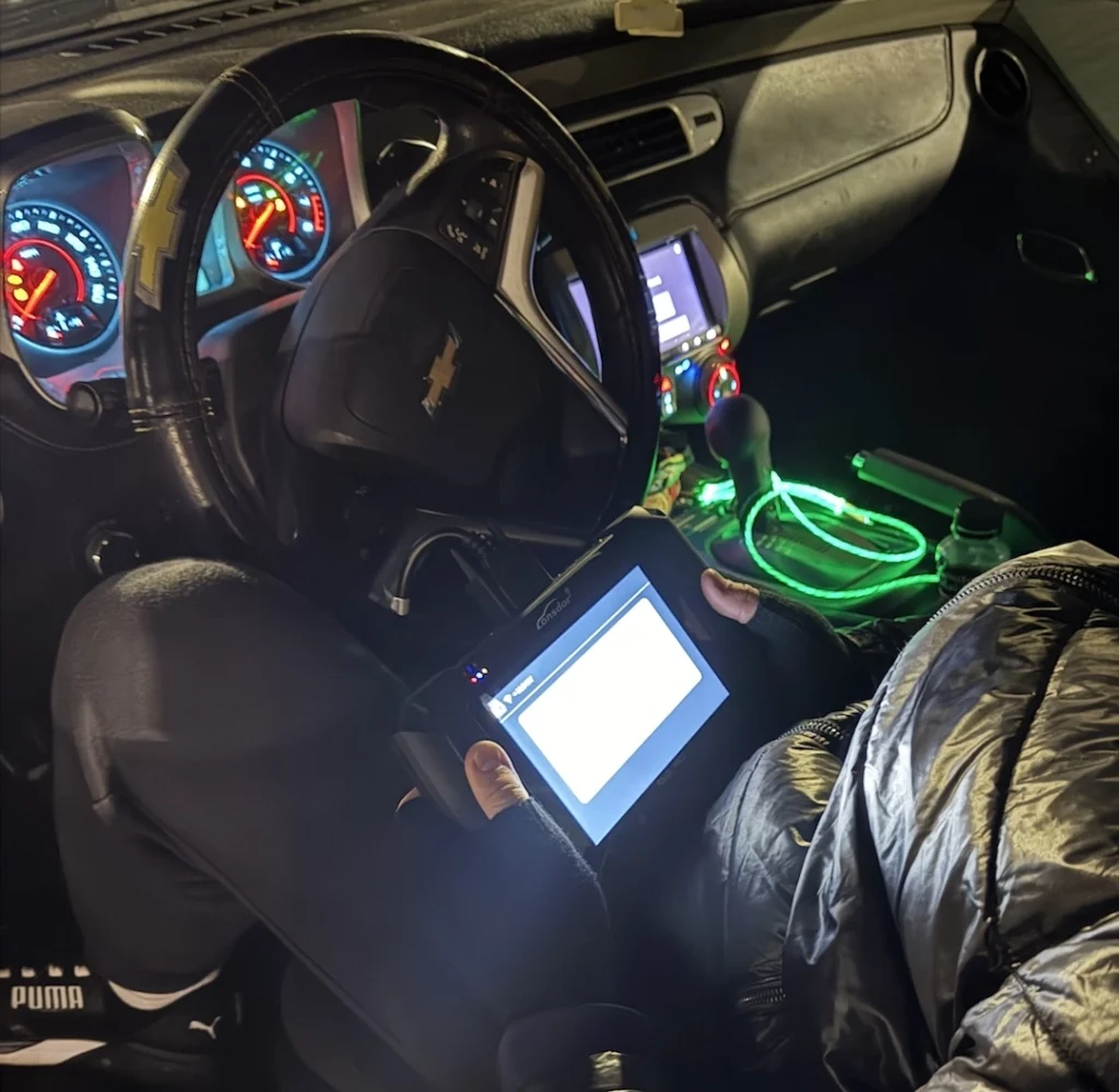 Mobile locksmith programming a new car key for a Chevrolet vehicle using a diagnostic tool at night in Charlotte, NC.